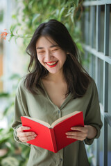 Joyful Woman Laughing While Reading a Red Book &ndash; Happiness and Learning