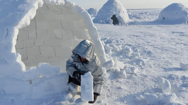 A happy adult woman builds an Igloo out of snow blocks in the Eskimo Village.