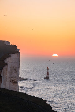 Sunrise behind beachy head lighthouse during hide tide on the south downs east Sussex south east England UK