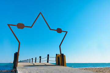 Obraz premium Wooden pier on sea stretching into distance beyond horizon with beautiful star shaped frame on sunny summer day. Vacation and Travel Concept.