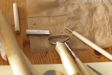 Close-up of clay sculpting tools, rolling pin, and clay on a wooden surface.
