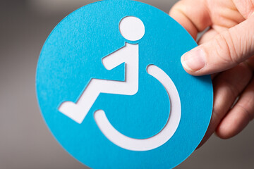 Close-up of a hand holding a blue card with a white accessibility symbol.