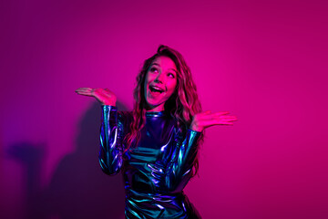Joyful young woman girl in glossy blue dress posing under bright pink neon light