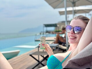 Jeune femme en bikini turquoise buvant une canette à côté d'une piscine débordante sur fond...
