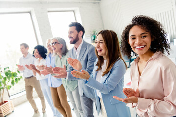 Diverse group of professionals applauding in an office environment filled with daylight and a collaborative atmosphere