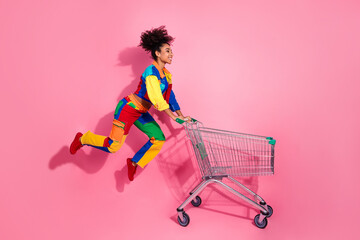 Vibrant young woman posing playfully with shopping cart against pink background