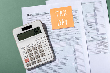 Inscription Tax day on orange sticker and white calculator on individual income tax return form 1040