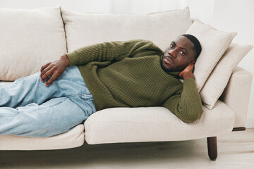 Relaxed man in a green sweater lounging on a light colored sofa, showcasing comfort and style in a bright indoor setting