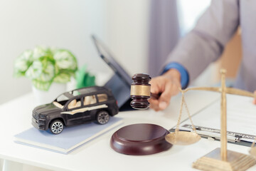 Judge and miniature car symbolize auction or court action against driver who has accident and receives insurance payment, car with scale and hammer on table