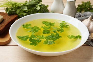 Tasty chicken bouillon in bowl with bread and ingredients on wooden table, closeup