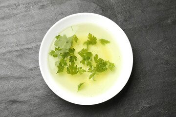 Tasty chicken bouillon with parsley in bowl on black table, top view