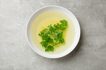 Tasty chicken bouillon with parsley in bowl on grey table, top view