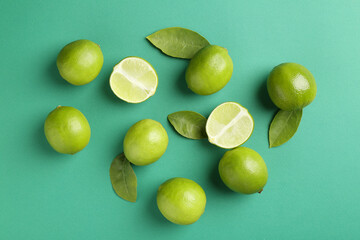 Many fresh limes and leaves on green background