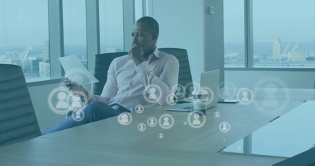 Image of media icons over african american businessman reading document in office