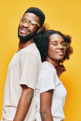 Obraz premium Two smiling models with glasses in casual outfits against a vibrant yellow background, showcasing a youthful and positive vibe