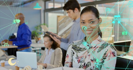 Image of network of connections with icons over diverse colleagues working in office