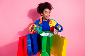 Smiling young woman holding colorful shopping bags against a pink background, showcasing joy and...
