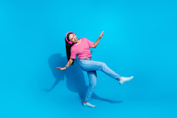Obraz premium Woman in casual outfit dancing with headphones against vibrant blue background promoting lively and cheerful lifestyle