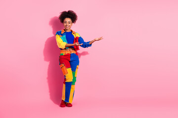 Cheerful young woman in vibrant patchwork outfit posing against a pink studio background