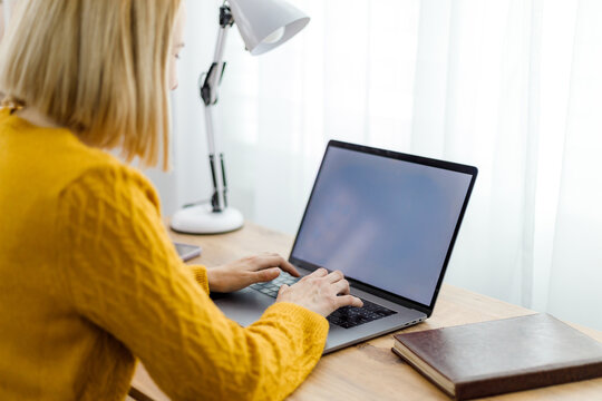 Woman working on laptop at a sunny desk with books