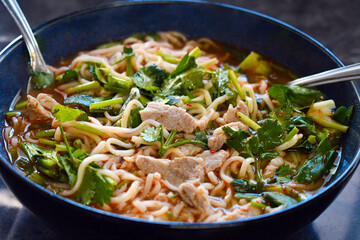 Spicy noodles with pork, seasonings and coriander in a bowl.