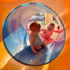 Bébé et enfant dans un tube d'une aire de jeux au soleil © Mathieu