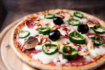 Pizza with salami and mozzarella cheese, jalapeno pepper and black olives. Wooden background. Soft focus. Close up.	
