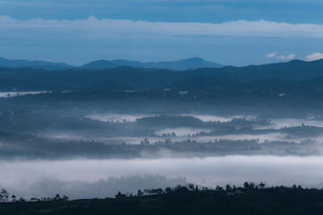 blue sunrise in the hills where you can see some lights of houses among the fog in the valleys.