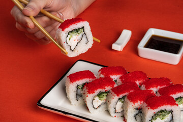 California rolls with red tobiko on plate with soy sauce on orange background