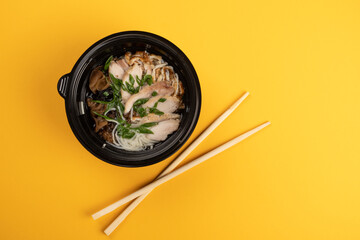 Delicious asian ramen in black bowl with chopsticks on yellow background