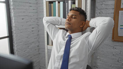 Fototapeta premium Handsome man relaxing in office indoors with hands behind head after a long workday