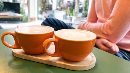 A vibrant orange cappuccino cup placed in the foreground with a man softly blurred in the background. Ideal for use in cafe marketing, personal well-being articles, or coffee culture content.