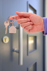 Eine Hand hält als Angebot einen Hausschlüssel vor einer Haustür