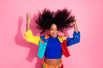 Vibrant young woman embracing joy and style with colorful attire and expressive gestures against a cheerful pink background.