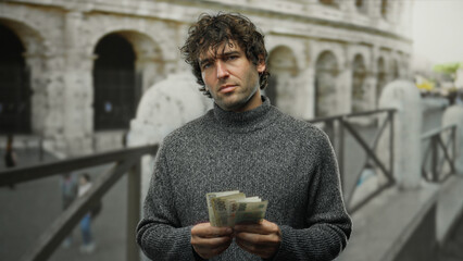 Hispanic man holding czech koruna banknotes stands outdoors in front of the iconic roman colosseum,...