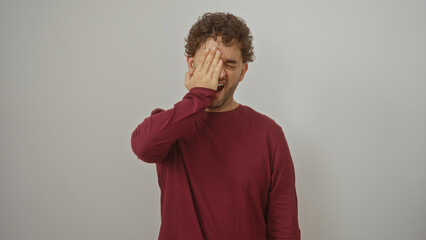 Young hispanic man covering face with hand in a maroon shirt against isolated white background...