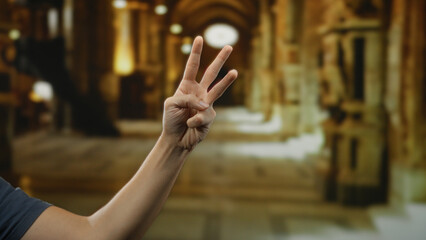 Hand of man indoors at museum room showing three fingers with blurred historical background highlighting architectural details and cultural atmosphere.
