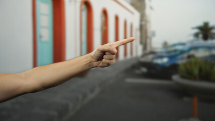 Obraz premium Man's hand pointing forward on a lively city street highlighting urban architecture and vibrant atmosphere, focusing on interaction and guidance outdoors in bustling surroundings.