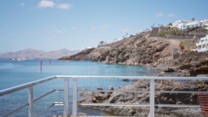 Naklejka premium Blurred coastal view in lanzarote, canary islands, showing rocky shoreline and distant boats against a clear blue sky