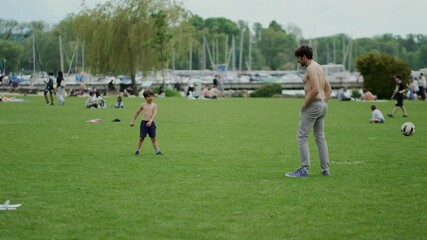 Father and son launch toy airplane in park, enjoying playful bonding on a sunny day. Surrounded by green grass and families, they share an exciting and memorable outdoor moment