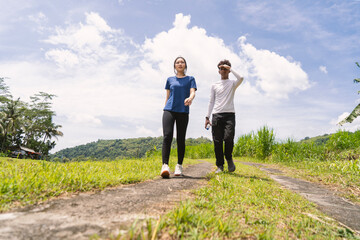 active young asian couple holding water bottle while walking exercise at rural area