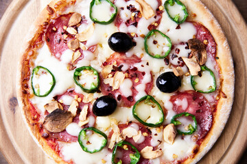 Pizza with salami and mozzarella cheese, jalapeno pepper and black olives. Wooden background. Soft focus. Top view. Close up.	