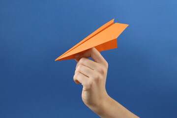 Woman with orange paper plane on blue background, closeup