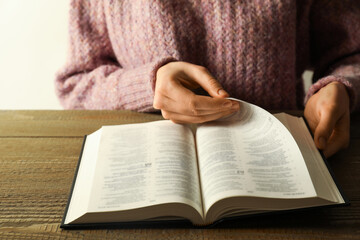 Naklejka premium Woman reading Holy Bible in English language at wooden table, closeup