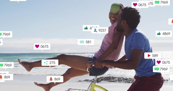 Riding bicycle on beach, social media notifications image over couple - Powered by Adobe