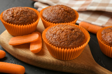 Delicious carrot muffins with fresh vegetables on black table, closeup