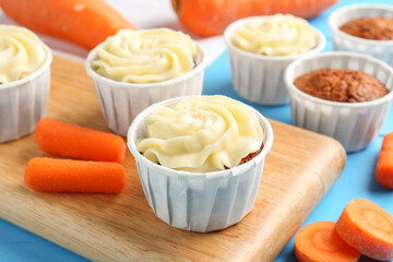 Tasty carrot muffins with fresh vegetables on light blue table, closeup