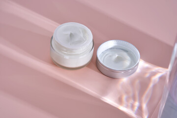 An open jar of cream with its texture on a pink background.