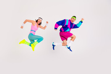 Energetic couple in vibrant retro workout attire jumping excitedly against a white background,...