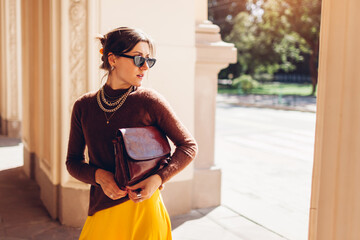 Portrait of young woman wears brown cashmere sweater and yellow skirt outfit on city street with...